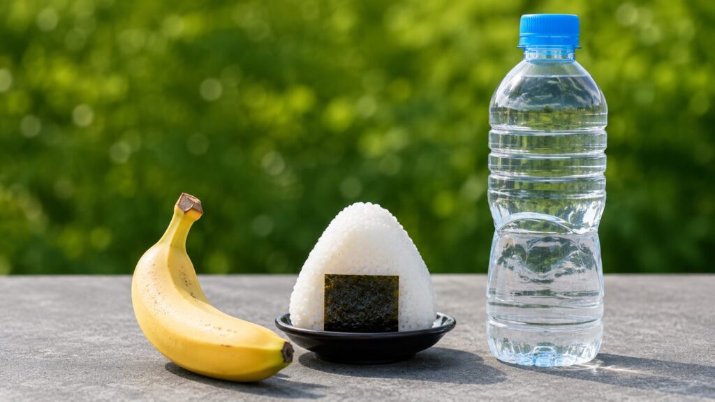 屋外の台に置かれたバナナとおにぎり、水入りボトルを用意した試合後の補食と水分補給