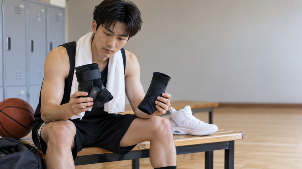 ベンチに座り、厚みや形状の異なる2種類の足首サポーターを手に取って見比べる選手